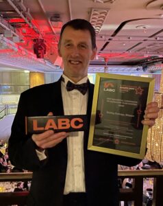 Richard Dawson, architect, at the LABC Grand Finals holding the trophy and certificate for winning the LABC 2023 Best Residential Conversion or Alteration to an Existing Home,